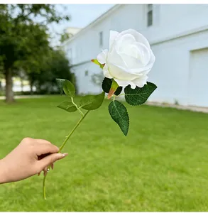 Detail view of a white artificial rose held by hand against a green lawn background