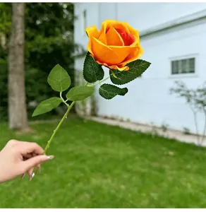 Hand holding a single artificial orange rose against a green lawn background