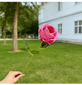 Single branch artificial pink rose being held in a natural garden setting