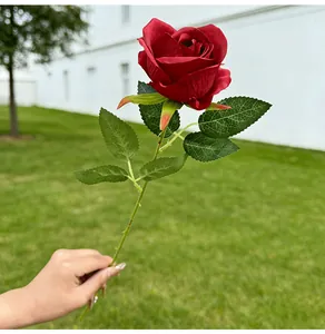 Close-up of a hand holding a single stem red artificial rose with realistic leaf detail