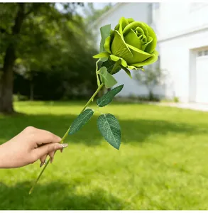Detailed view of a single artificial green rose held against a blurred outdoor background.