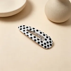 Close-up of a white snap hair clip with black polka dots on a beige background
