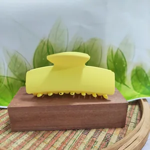 Close-up of a vibrant yellow rectangular matte hair claw clip on a wooden stand.