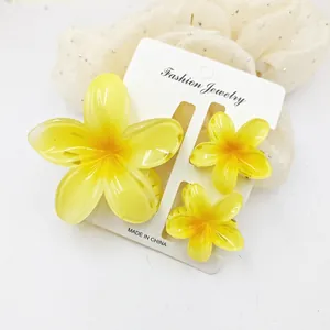 Detail view of three vibrant yellow frangipani flower hair clips on a jewelry card.