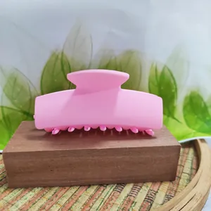Close-up of a matte pink rectangular hair claw clip on a wooden display block