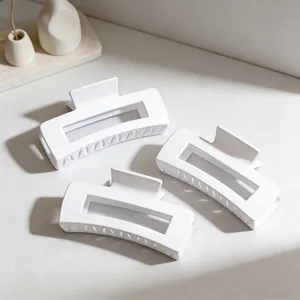 Close-up of three white matte rectangular hair claw clips on a minimalist surface