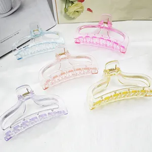 Five colorful transparent pastel plastic hair claw clips arranged on white fabric background