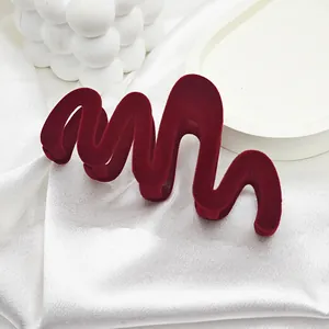 Elegant macro view of a large wavy deep red velvet hair claw clip on white silk fabric