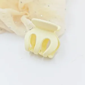 Close-up view of a matte yellow small hair claw clip placed on soft fabric background