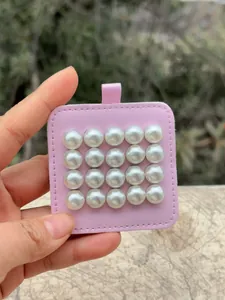 Vista detallada de 16 pendientes de perlas magnéticas en una pequeña tarjeta rosa.