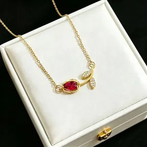 Elegant gold tulip pendant necklace with red gemstone detail on white jewelry box