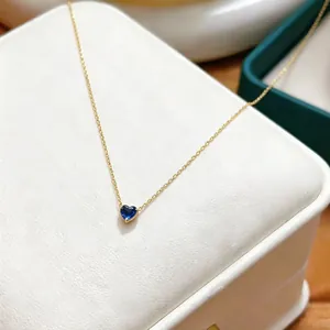 Macro detail shot of a dainty blue heart-shaped birthstone pendant on a gold chain necklace.