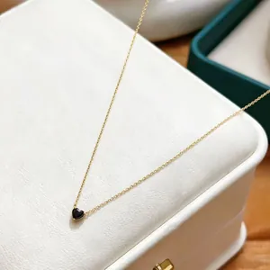 Close-up detail of a dainty gold chain necklace with a black heart-shaped pendant charm.