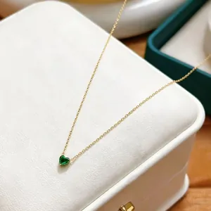 Detailed macro shot of a gold heart pendant necklace with a green emerald birthstone