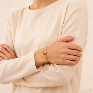 Bracelet élégant à breloque cœur en or porté au poignet d'un mannequin en haut beige