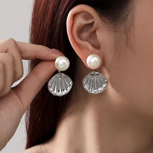 Detailed view of elegant silver sea shell earrings with large white pearls worn by a model