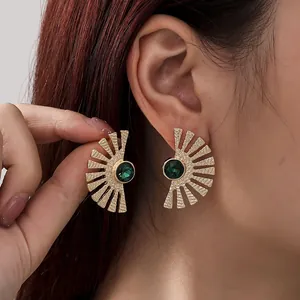 Macro detail of elegant gold fan-shaped earrings with deep green crystal centers