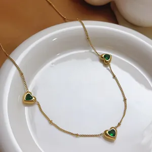 Detail van gouden roestvrijstalen ketting met drie smaragdgroene hartvormige hangers.