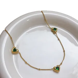 Detailweergave van drie hartvormige smaragdstenen aan een gouden roestvrijstalen ketting.