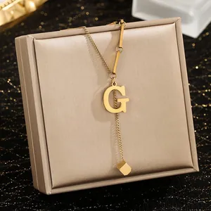 Detailopname van gouden roestvrijstalen ketting met G-letter en kubusvormige hanger
