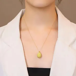 Detailed view of a golden durian pendant necklace worn by a model in a white blazer.