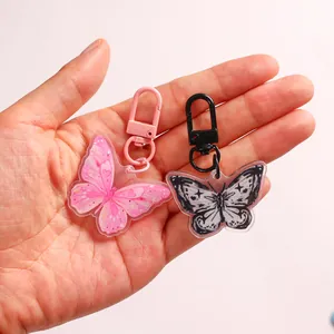 Pair of cute butterfly acrylic keychains in pink and black colors held by hand
