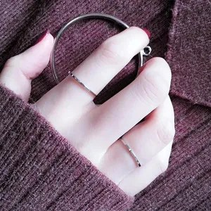 Detailed view of minimalist silver thin rings worn on a hand against a maroon knit sweater.