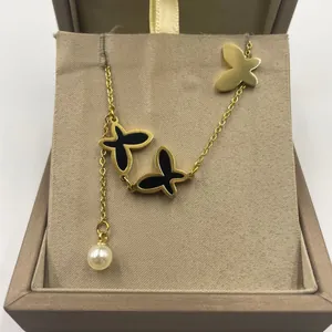 Détail d'une chevillère papillon dorée avec incrustation noire et breloque en perle blanche.