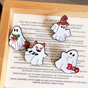Detailed macro view of four unique Halloween ghost enamel pins displayed in a wooden tray