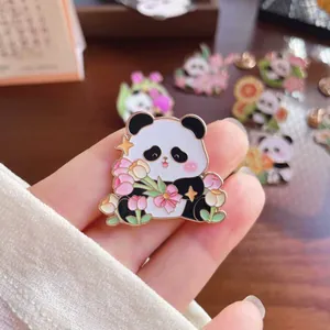 Detailed macro view of a cute cartoon panda enamel pin with pink flowers held in hand