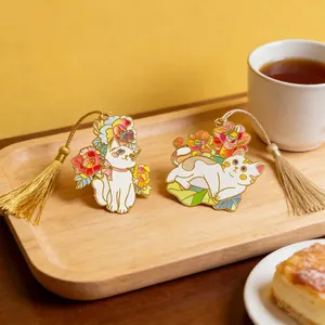 Detailed view of two cute enamel cat bookmarks with golden tassels on a wooden tray