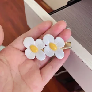 Detailed view of cute white daisy flower hair clips held in hand showing texture.