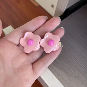 Detailed close-up view of glossy pink candy-colored flower hair clips held in hand