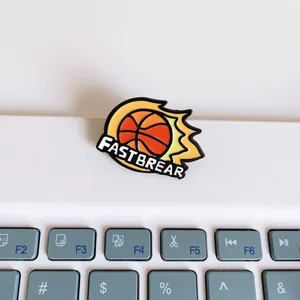 Detailed view of a flame basketball enamel pin with FASTBREAR text on laptop keys