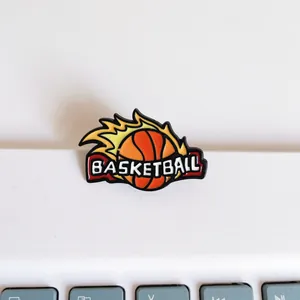 Close-up of a flaming basketball enamel pin with white lettering on a textured surface.