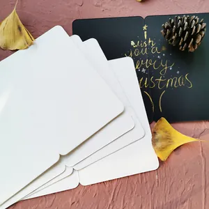 Pila de tarjetas DIY blancas y negras con mensaje navideño dorado sobre fondo marrón.