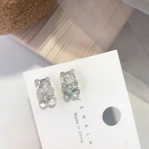 Detalle macro de pendientes de oso de gominola holográficos iridiscentes en tarjeta.
