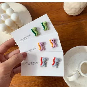 Gros plan de boucles d'oreilles dinosaure de dessin animé en vert, rose et gris