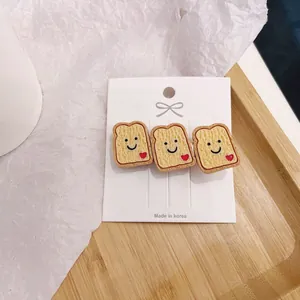 Close-up of three cute simulation bread toast hair clips with smiley faces on a card