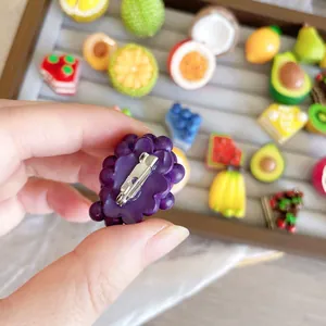 Close-up detail of a cute purple resin grape brooch showing the silver safety pin backing