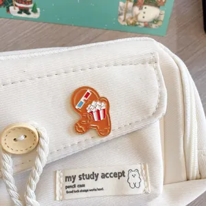 Close-up detail showing a cute gingerbread man enamel pin on a white corduroy bag.