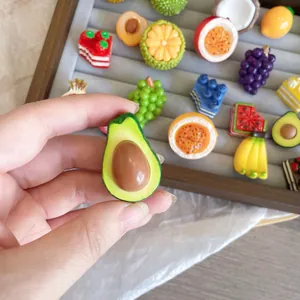 Detailed close-up of a 3D resin avocado brooch held by hand among other fruit pins