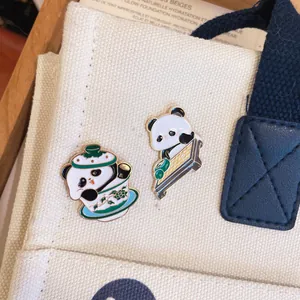 Dettaglio ravvicinato di due simpatiche spille in smalto a forma di panda su borsa di tela.