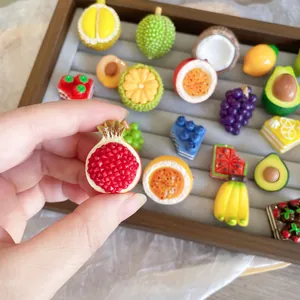 Close-up of a realistic resin pomegranate pin with various fruit badges in the background.
