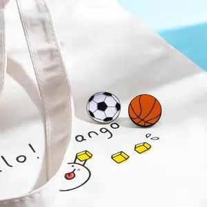 Close-up detail of soccer and basketball enamel pins on a white canvas tote bag