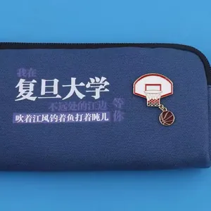 Close-up detail of a basketball hoop and ball enamel brooch on a blue fabric pouch.