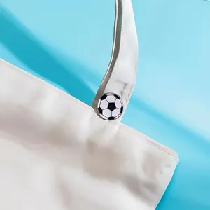 Detail of a classic black and white soccer ball enamel pin on a white canvas tote bag.