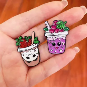 Close-up of cute strawberry and grape fruit milk tea cup cartoon enamel pins on a hand