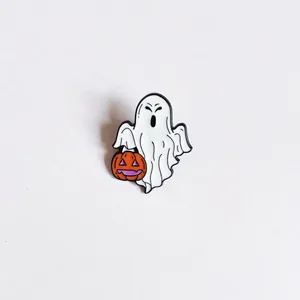 Close-up detail of a cute Halloween ghost enamel pin holding a small pumpkin lantern.