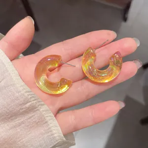 Primo piano di orecchini in acrilico iridescenti a forma di C tenuti in mano